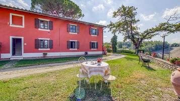 A red villa with a garden, a table with chairs, and a view of the countryside.