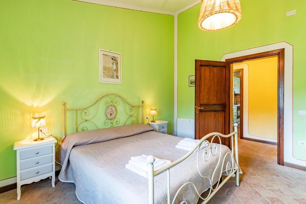 A bedroom with a bed, nightstands, a lamp, a door, and a wall with a picture.