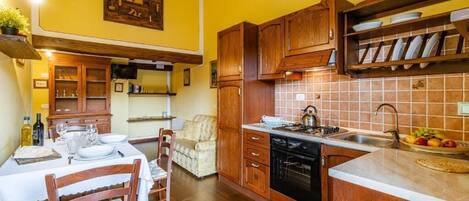 A compact kitchen with wooden cabinets, a tiled backsplash, and a dining area with a table set for two.