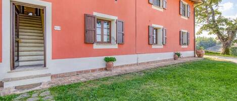 Un edificio rojo con base blanca, numerosas ventanas con persianas, un camino de piedra y un césped.