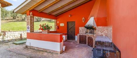 An outdoor patio with a barbecue area, a stone wall, and a wooden pergola.