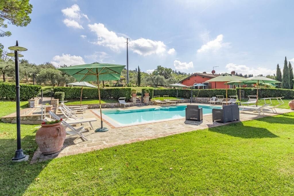 A swimming pool with lounge chairs and umbrellas, surrounded by a well-maintained lawn and hedges.