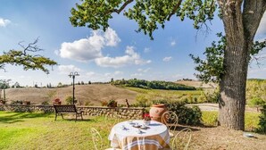 A round table with a striped tablecloth, surrounded by metal chairs, set in a grassy outdoor area with a stone wall and potted plants. - Agriturismo Rebarco (Castelfiorentino)