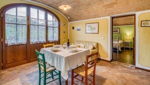 A dining area with a table set for four, wooden chairs, a brick ceiling, and a large window with lace curtains. - Agriturismo Rebarco (Castelfiorentino)