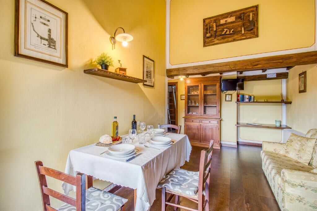 A dining area with a table set for four, wooden chairs, a wooden cabinet, and a sofa in the background.