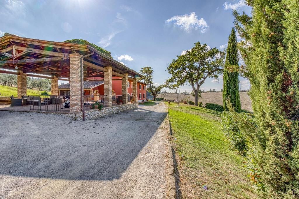 A covered outdoor area with a gravel path leading to a building with a red facade and a stone foundation.