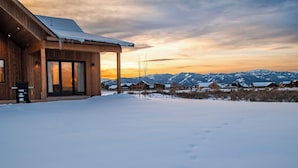 Une cabane en bois dotée d’un patio couvert, avec un sol enneigé et un paysage montagneux en arrière-plan.
