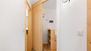 A narrow hallway with wooden doors, a white wall, and a small shelf unit with a light switch. - Apartment 'Lory' with Mountain View and Balcony (Daldoss)