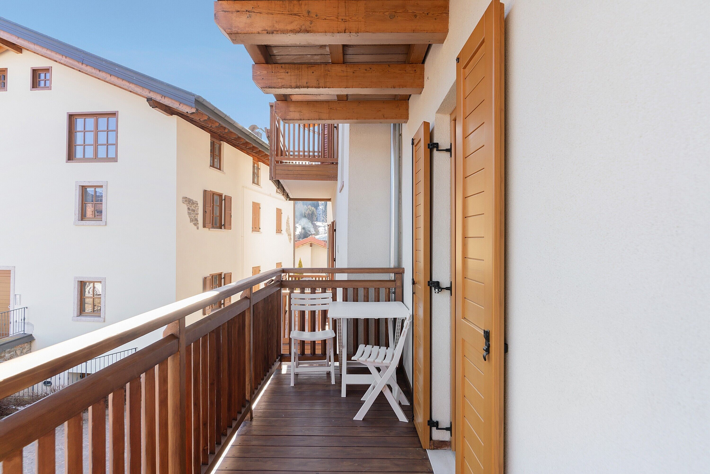 Ein Balkon mit Holzgeländern, einem weißen Tisch und zwei Stühlen.