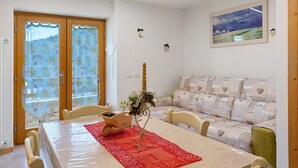A dining area with a table, chairs, a red runner, a decorative candle, and a sofa with patterned cushions. - Apartment 'Lory' with Mountain View and Balcony (Daldoss)