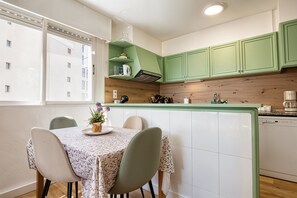 Eine moderne Küche mit grünen Schränken, einer Holzausziehtafel und einer Essecke mit einem Tisch für zwei Personen.