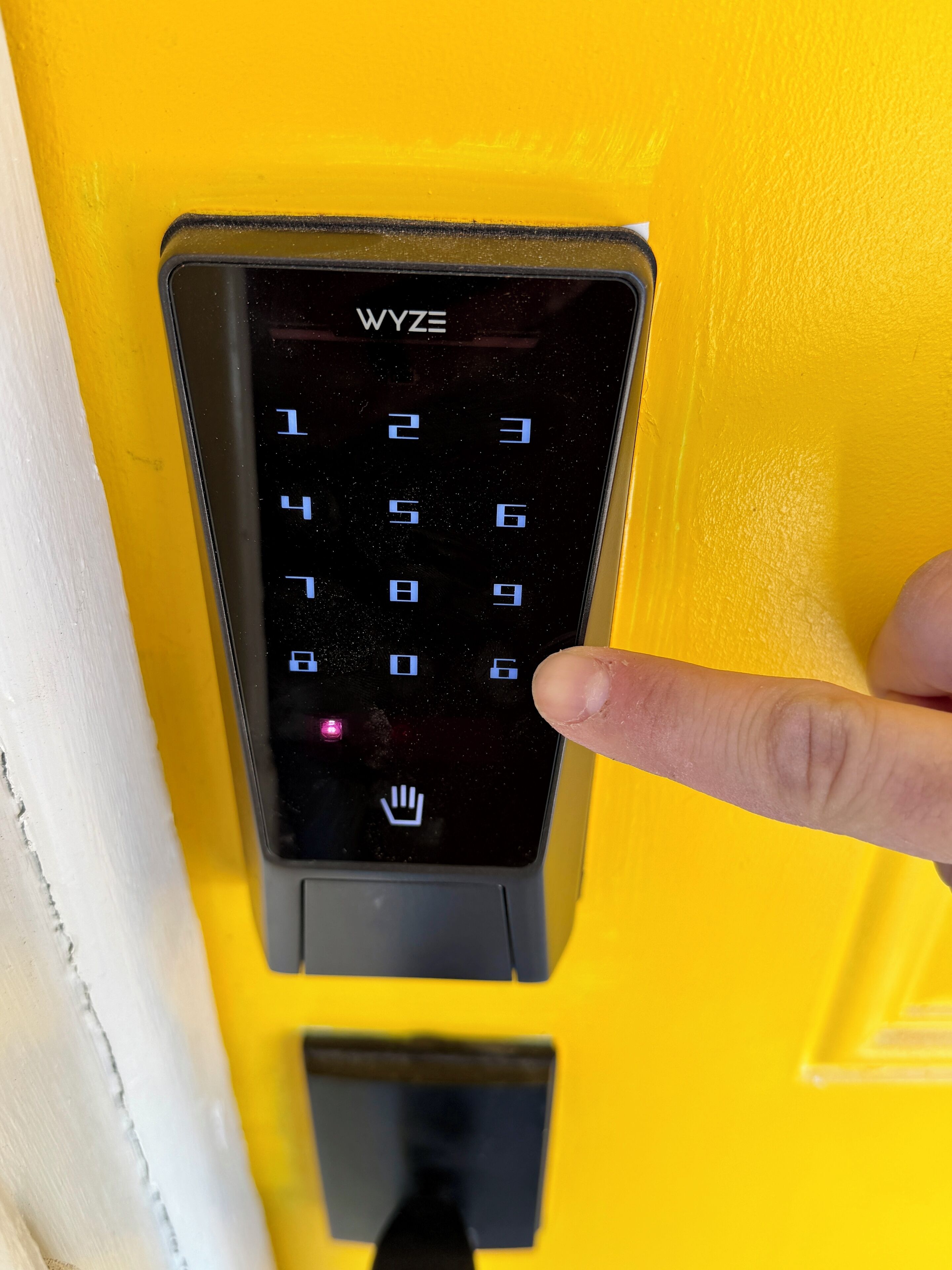 Une porte jaune dotée d’un clavier à code, sur laquelle une main appuie sur un bouton.