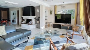 Ein modernes Wohnzimmer mit einer Couch, Sesseln, einem Fernseher und einem Kamin.