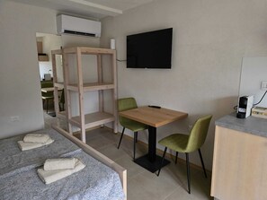 A small, modern room with a bed, a desk, two chairs, a TV, and a built-in shelf unit. - Razor Vista Apartments in the Soča Valley - STUDIO (Tolmin)