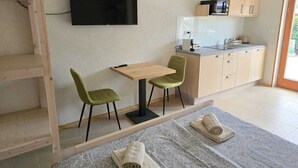 A compact hotel room with a kitchenette, a TV mounted on the wall, a small dining table with two chairs, and a bed with towels. - Razor Vista Apartments in the Soča Valley - STUDIO (Tolmin)