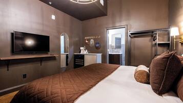 A hotel room with a large bed, a flat-screen TV, a vanity with a mirror, and a modern ceiling light fixture.