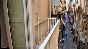 Ένας στενός δρόμος με κτίρια και στις δύο πλευρές, ένα μπαλκόνι με κάγκελο και μια πόρτα με τμήμα από γυαλί.