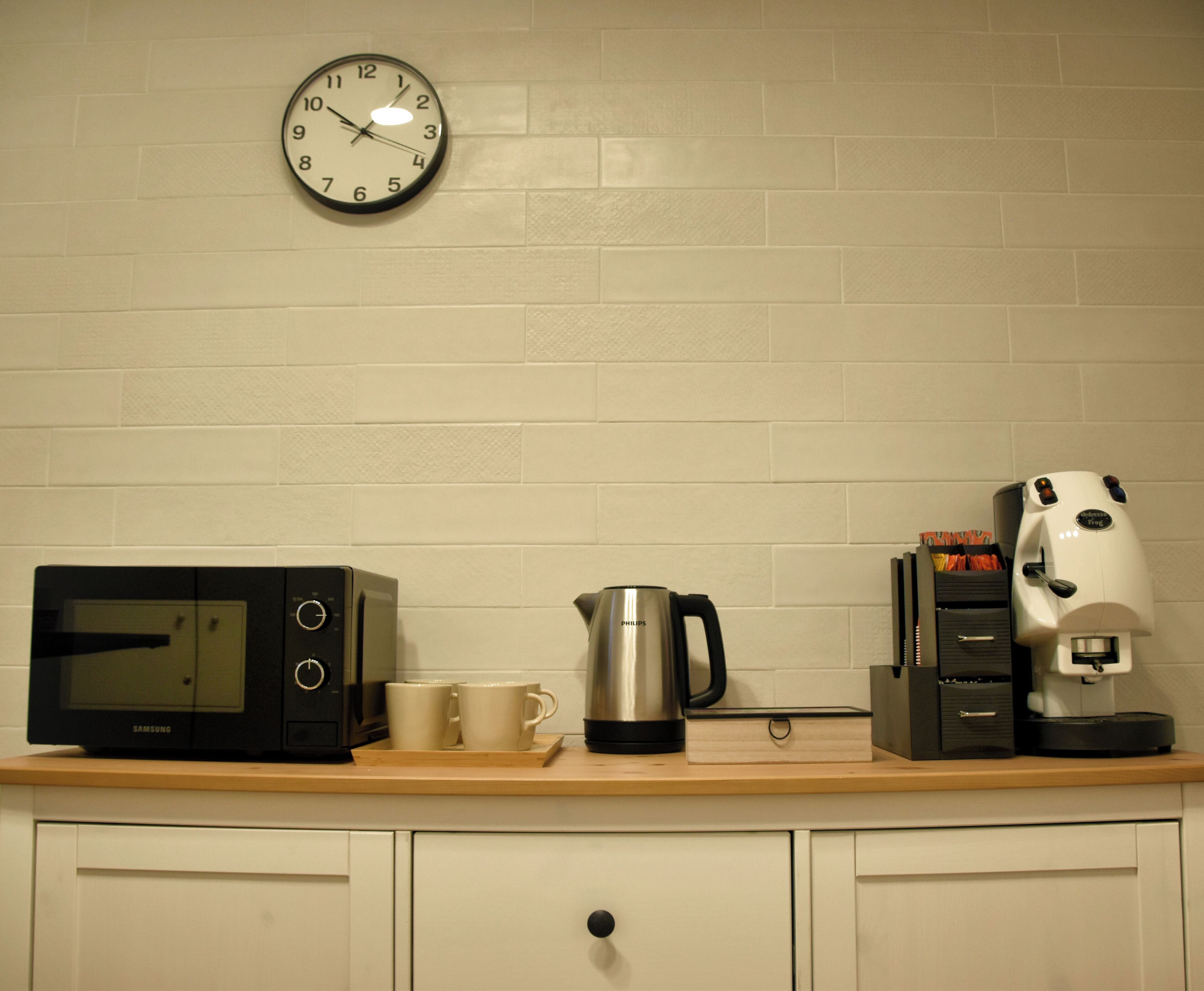 Un comptoir de cuisine avec un four à micro-ondes, une machine à café et une horloge au mur.