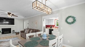 A modern living room with a fireplace, a dining table with green placemats, white chairs, and a ceiling fan. - 3 bedroom house in North Myrtle (North Myrtle Beach)