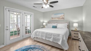 A bedroom with a bed, a ceiling fan, a nightstand with a lamp, a painting on the wall, and a door leading to a balcony. - 3 bedroom house in North Myrtle (North Myrtle Beach)