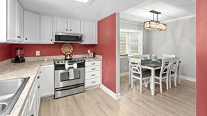 A modern kitchen with white cabinets, a stainless steel stove, and a dining area with white chairs and a table. - 3 bedroom house in North Myrtle (North Myrtle Beach)