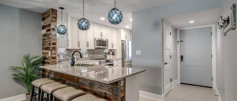 A modern kitchen with a central island, bar stools, hanging pendant lights, and a wooden accent wall.