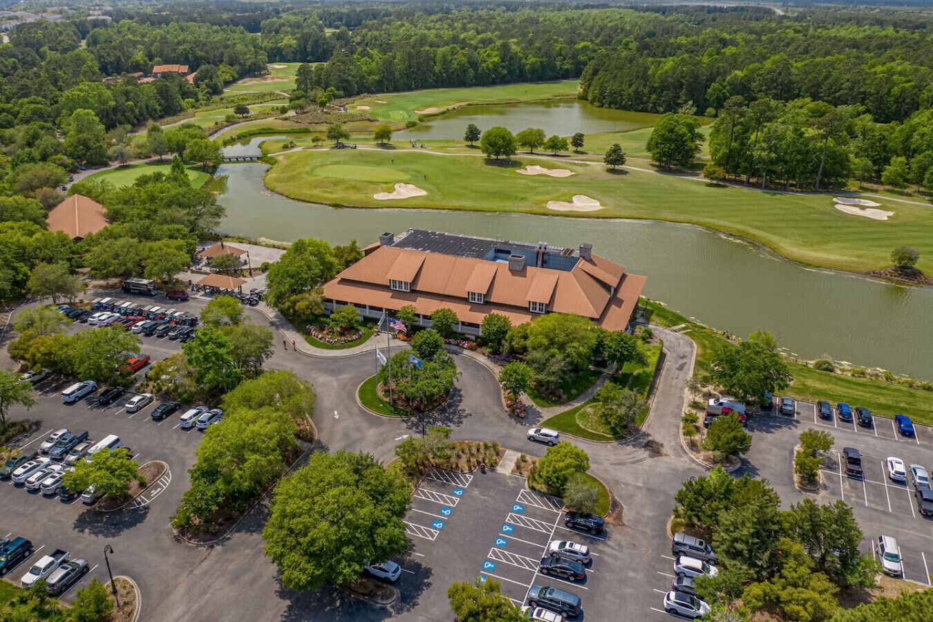 Vue aérienne d’un terrain de golf avec un club-house, un parking et la végétation environnante.
