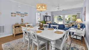 A dining area with a white table and chairs, a ceiling fan, and a large window with a view of the outdoors. - 3bedroom condo in Ocean Keyes, North Myrtle (North Myrtle Beach)