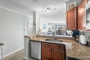 A modern kitchen with granite countertops, wooden cabinets, a stainless steel dishwasher, and a built-in oven. - Saltwater Serenity 3rd floor 2 bed 2 bath condo (North Myrtle Beach)