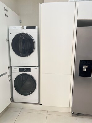 A laundry area with a Samsung washer and a Whirlpool dryer, a stainless steel refrigerator, and white cabinetry. - This gated community offer a Tranquil 1-bedroom condo with pool & 5 min to beach (Christ Church)
