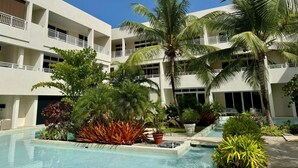 A hotel with a pool, palm trees, and a clear blue sky. - This gated community offer a Tranquil 1-bedroom condo with pool & 5 min to beach (Christ Church)
