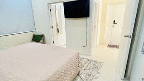 A bedroom with a bed, a flat-screen TV mounted on the wall, a door, and a rug. - This gated community offer a Tranquil 1-bedroom condo with pool & 5 min to beach (Christ Church)