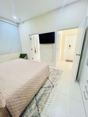 Ein Schlafzimmer mit einem Bett, einem flachbildfernseher an der Wand, einer Tür und einem Teppich.