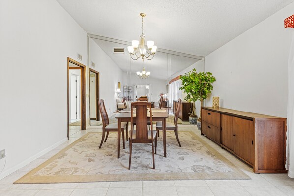 A spacious dining area with a wooden table and chairs, a chandelier, and a large mirror on the wall. - St Christopher's Retreat (Vero Beach)