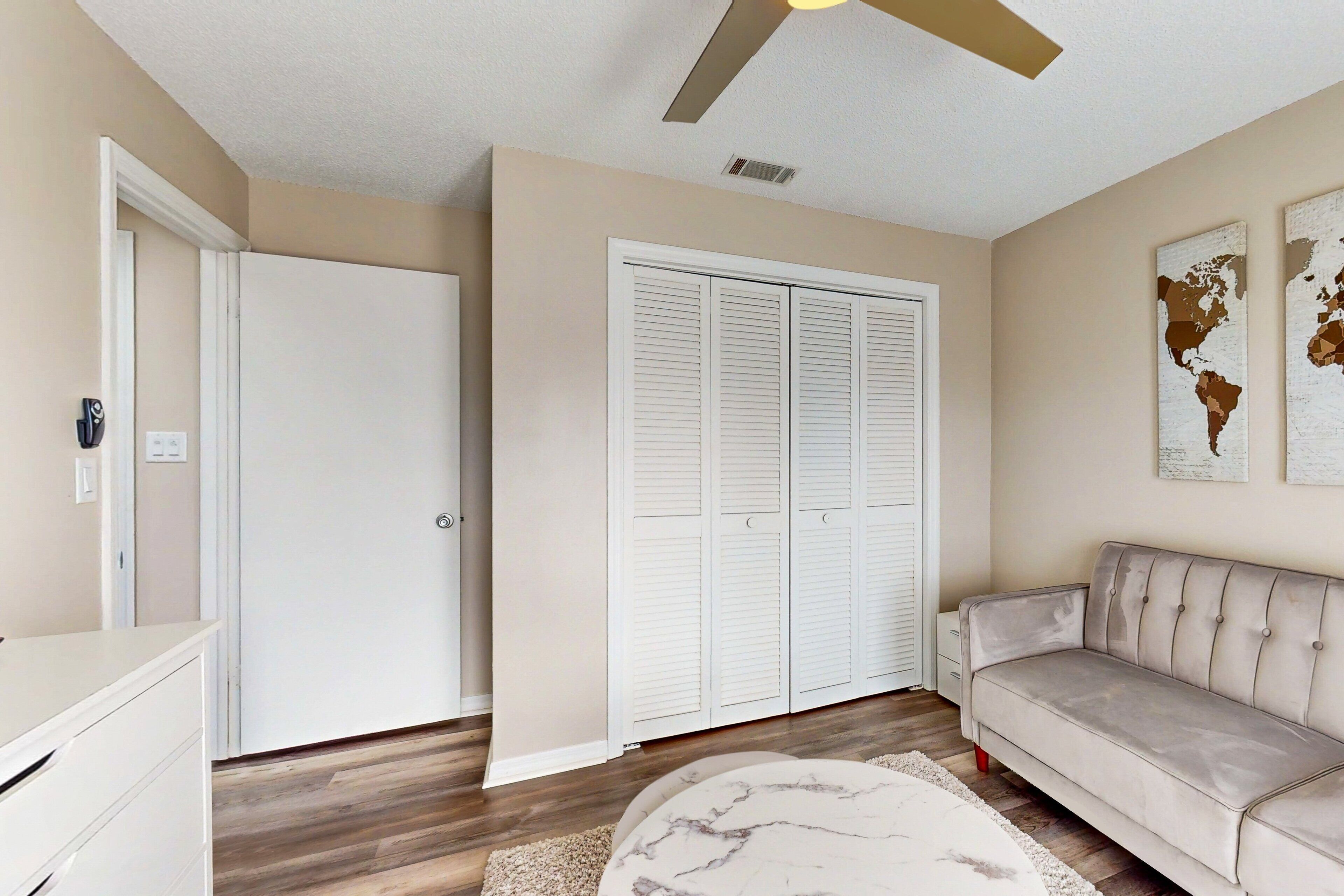 A living room with a beige sofa, a marble coffee table, a white wardrobe, and a ceiling fan.
