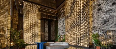 A modern lobby with a geometric patterned wall, a seating area, and potted plants.
