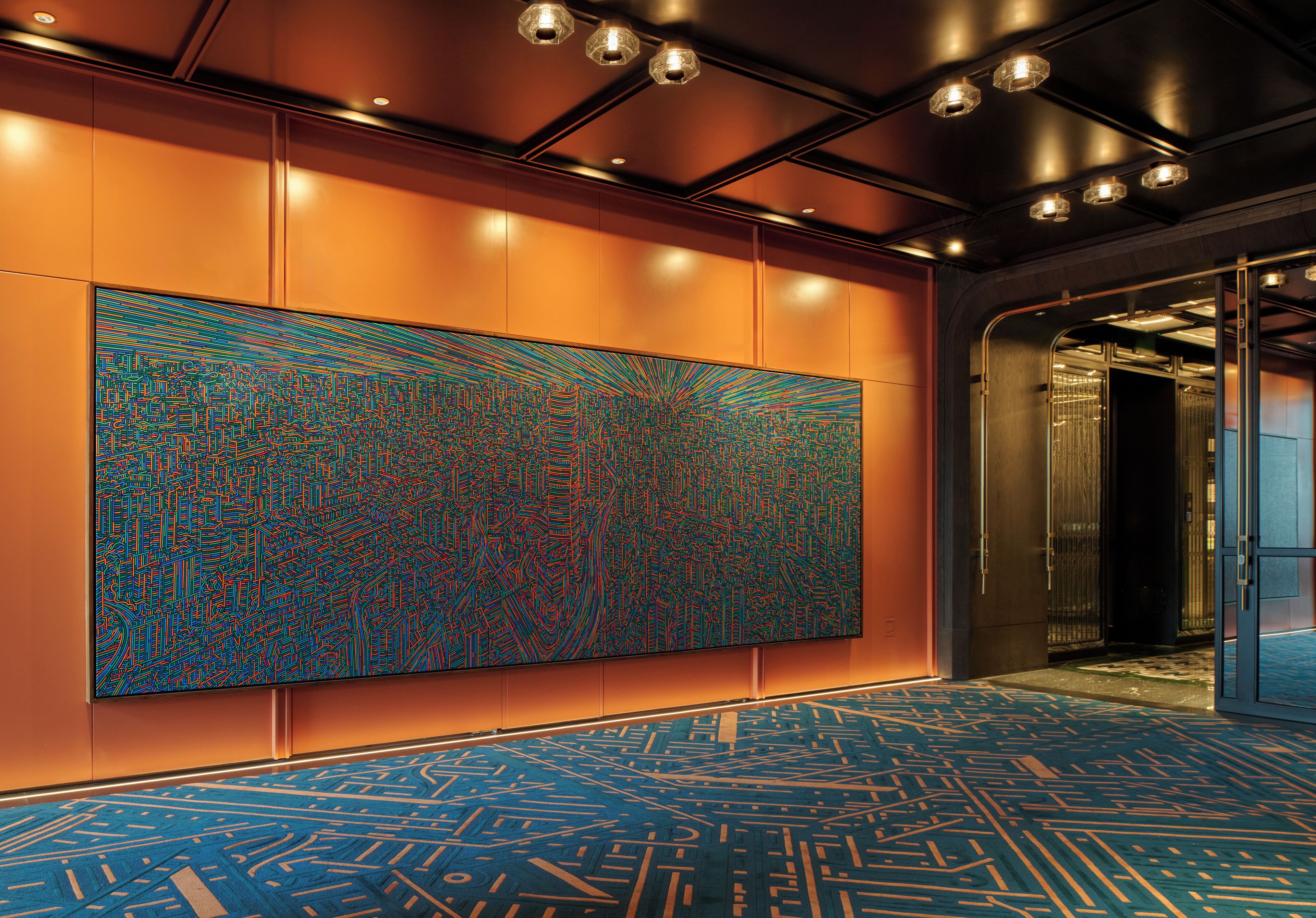Un hall d’entrée moderne, orné d’une grande œuvre d’art abstraite au mur, d’un tapis à motifs et d’une porte d’ascenseur en verre.