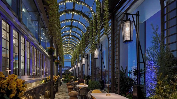 An indoor garden with tables and chairs, a wooden floor, and hanging plants. - Andaz Shanghai ITC (Shanghai)