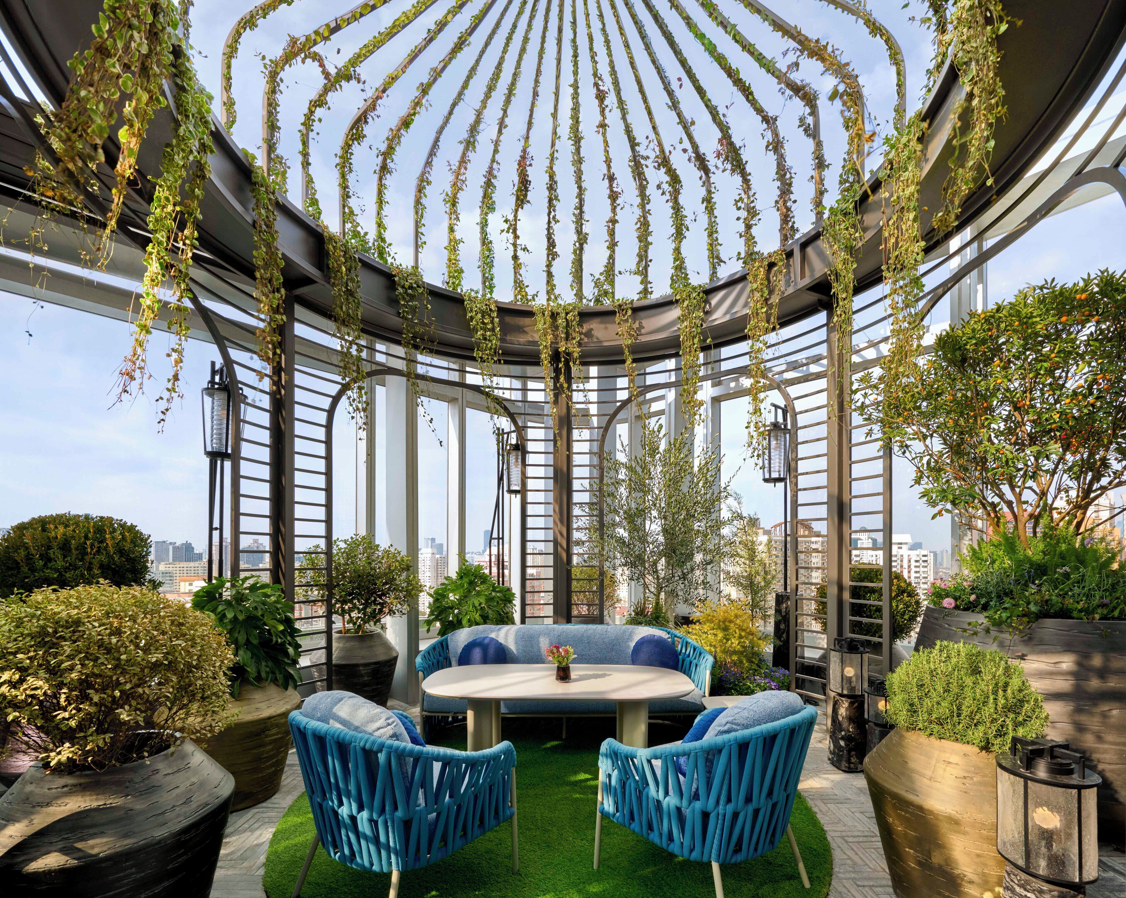 Un jardín en la azotea con una zona de estar circular, plantas en macetas y vistas de la ciudad.
