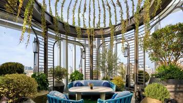 Un jardín en la azotea con una zona de estar circular, plantas en macetas y vistas de la ciudad.