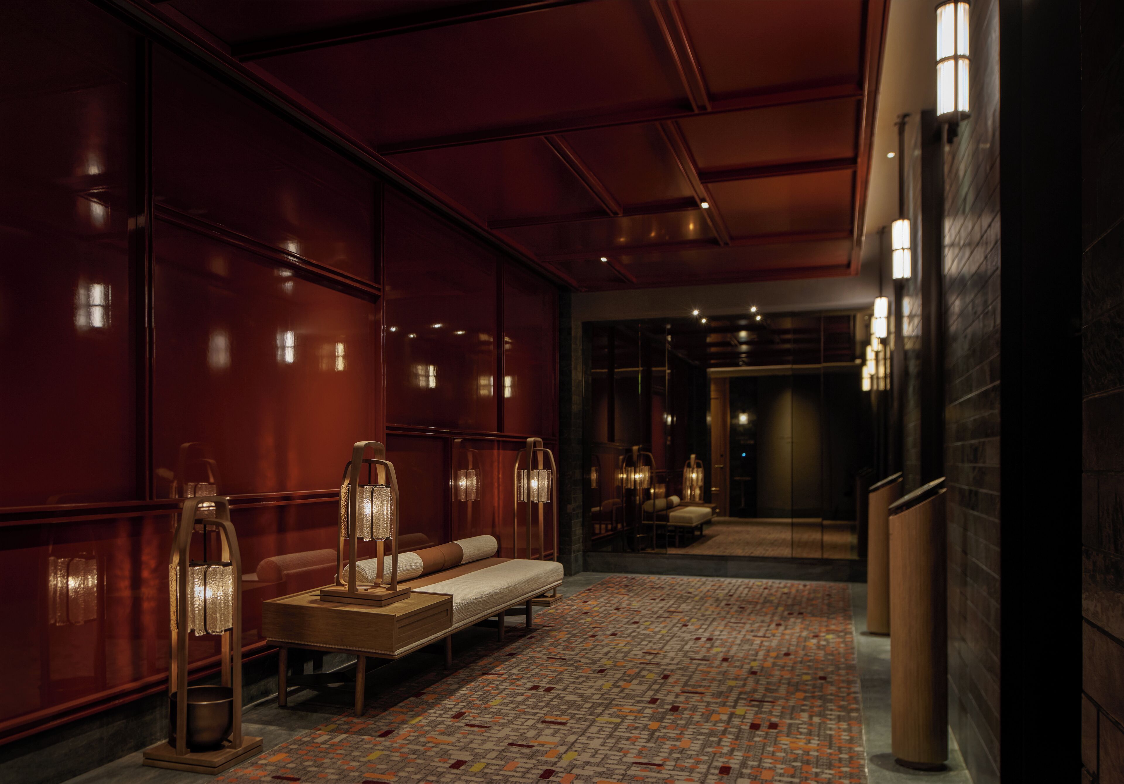 Un vestíbulo de hotel con alfombra estampada, un sofá y lámparas fijadas a la pared.
