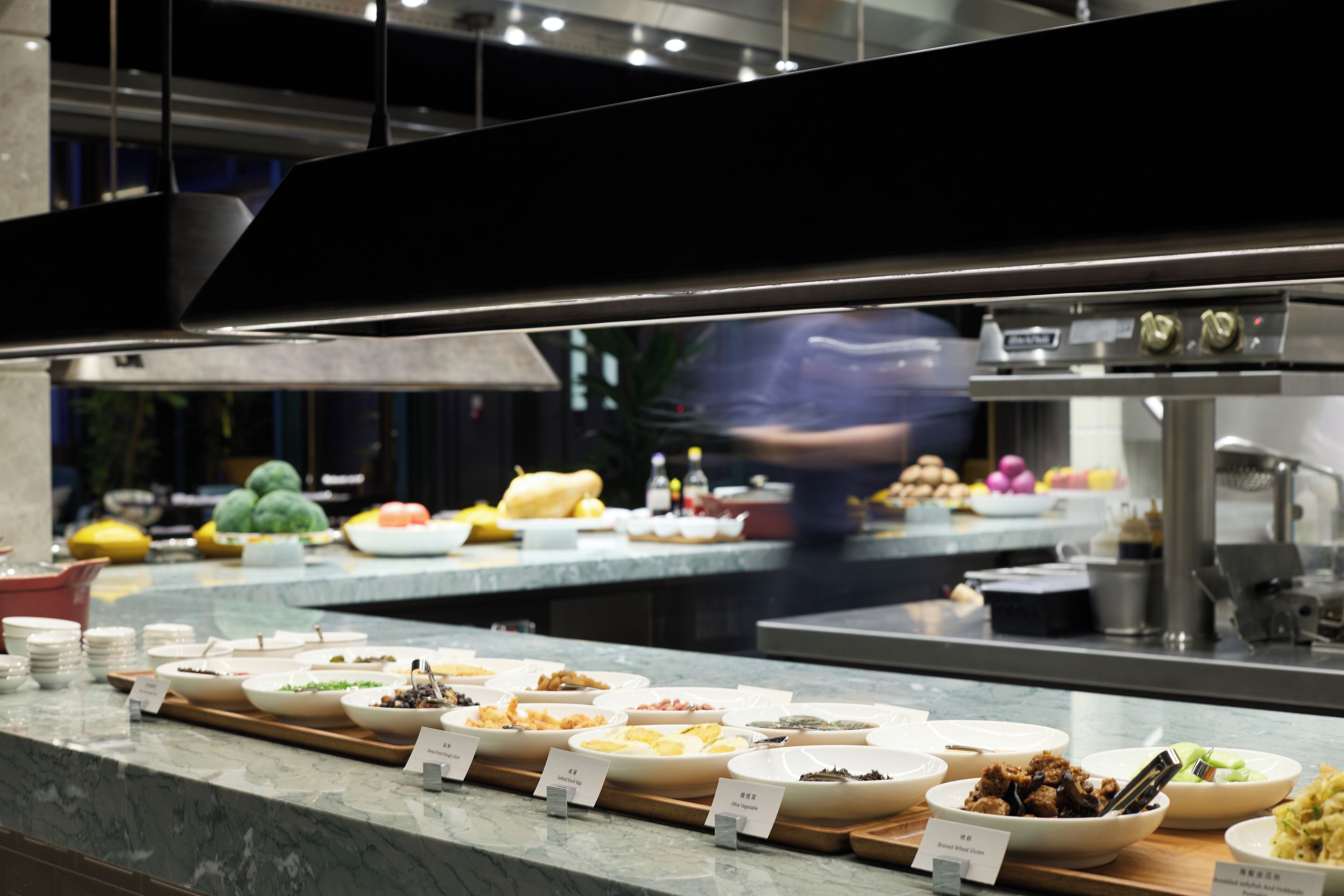 A buffet with various dishes and a kitchen area in the background.