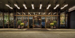 A hotel entrance with a glass facade, large potted plants, and modern lighting fixtures.