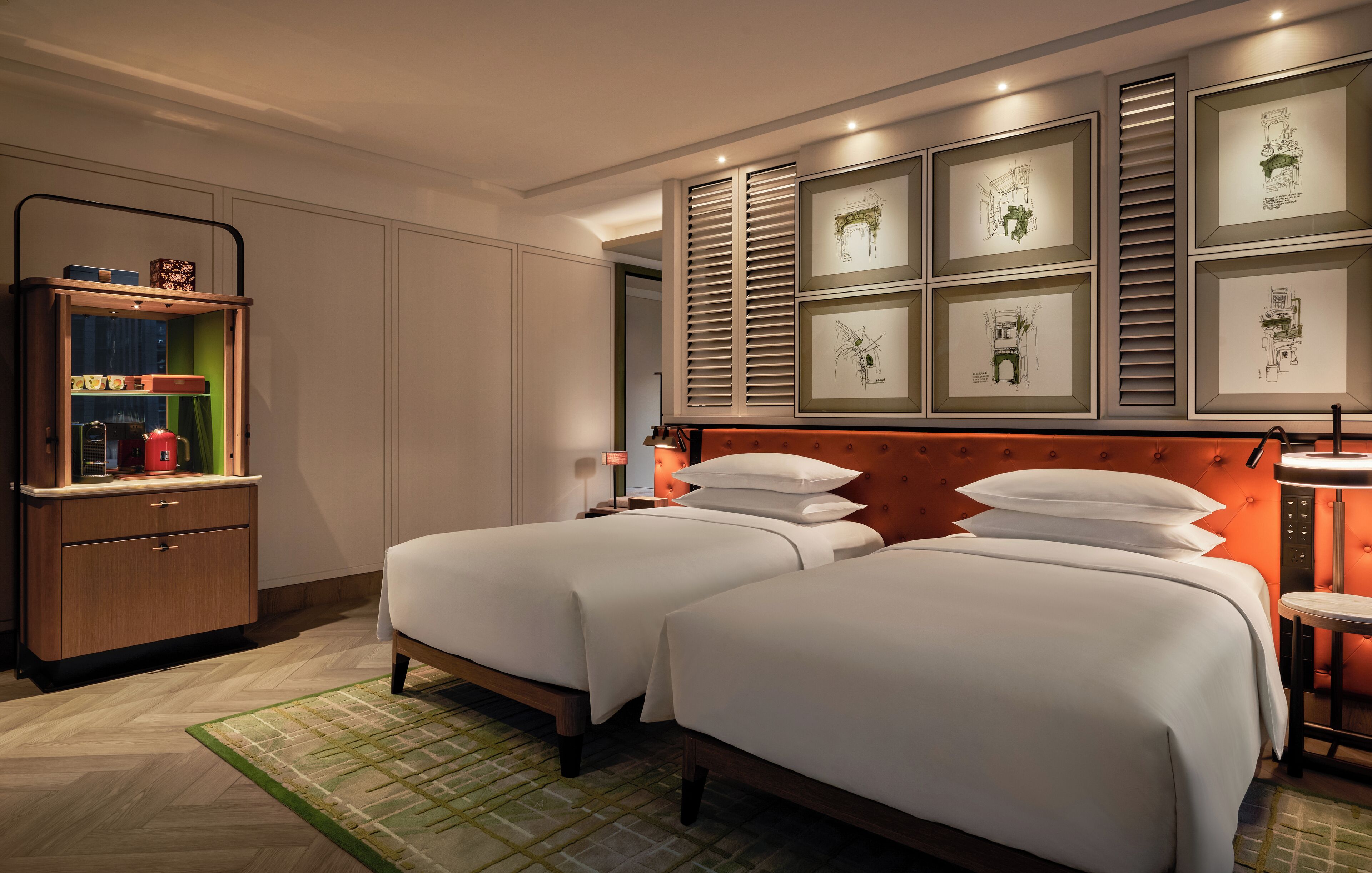 Une chambre d’hôtel avec deux lits, une armoire en bois et des dessins d’architecture encadrés accrochés au mur.