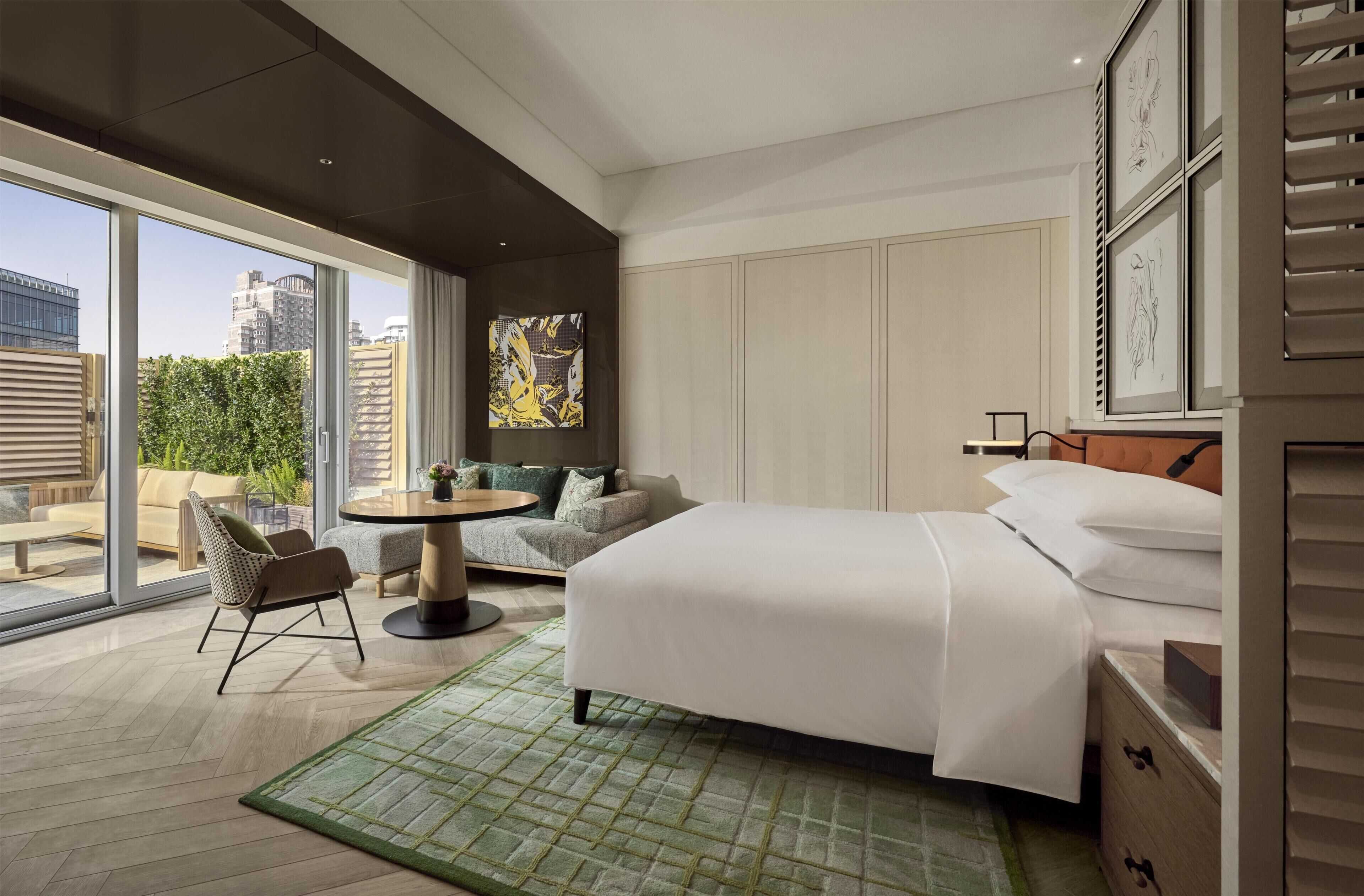 Habitación de hotel moderna con una cama grande, una mesa redonda, un sofá y vistas a la ciudad.