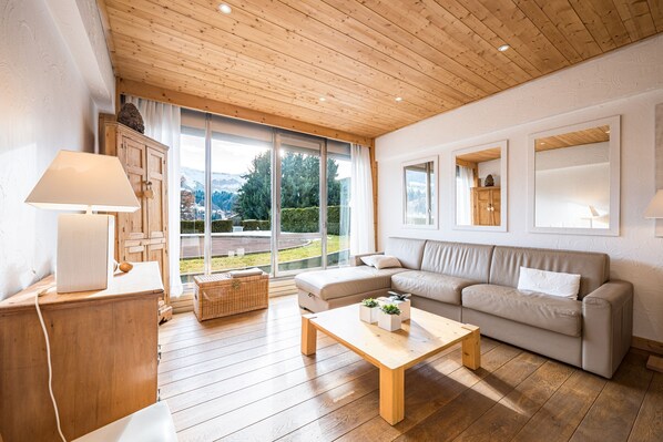 Een moderne woonkamer met een houten plafond, grote ramen, een bank, een salontafel en een houten kast.