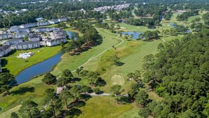 Ein Golfplatz mit einem großen Klubhaus, einem See und angrenzenden Wohngebieten.