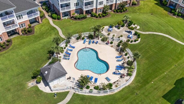 Luftaufnahme eines Wohnkomplexes mit einem zentralen Schwimmbecken, umgeben von Liegestühlen und einem eingezäunten Deckbereich.