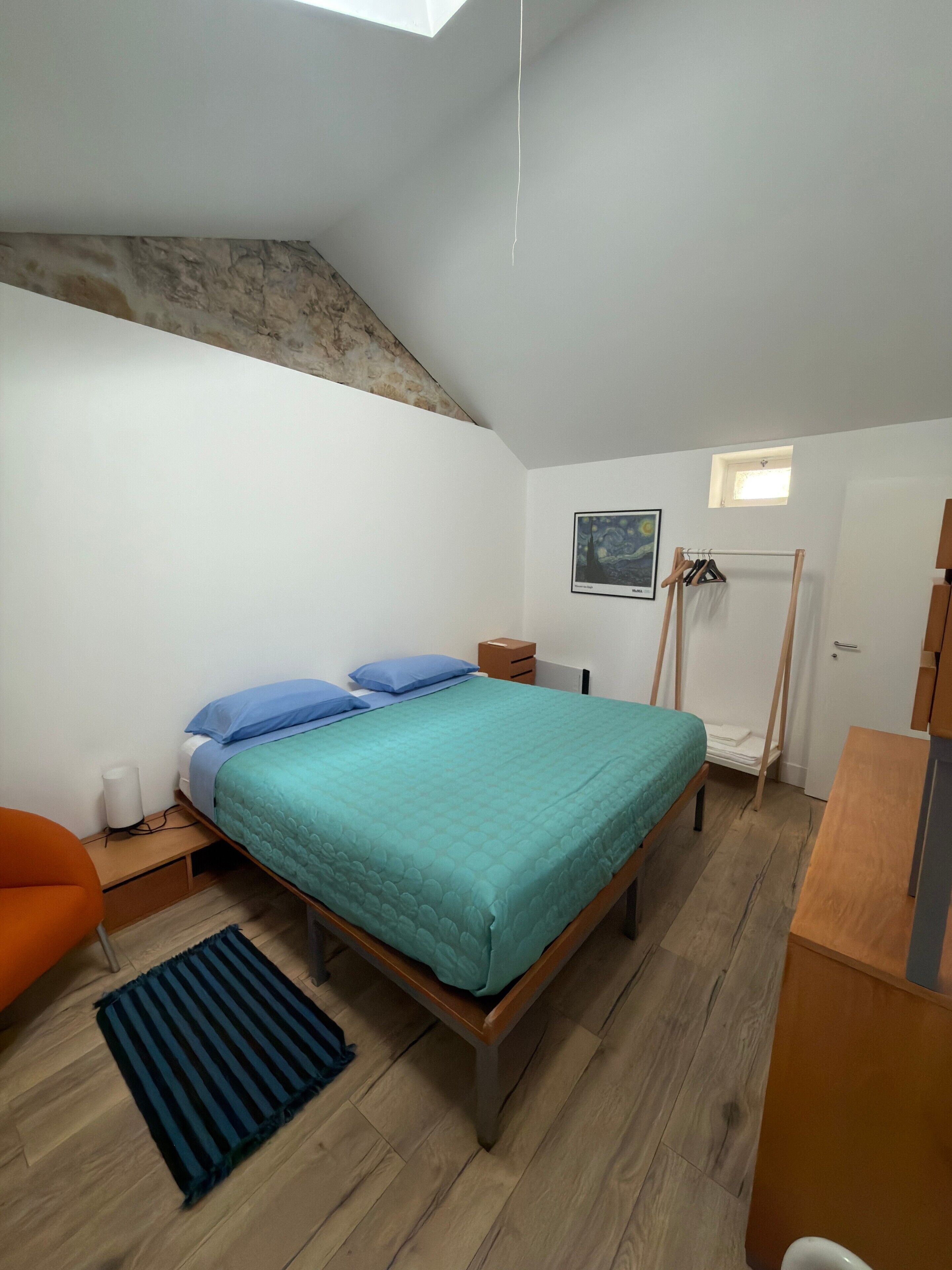 Une chambre à coucher comprenant un lit, un bureau, une chaise, un radiateur et une petite fenêtre.