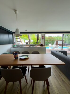A modern kitchen with a dining area, large windows, and a view of a swimming pool.
